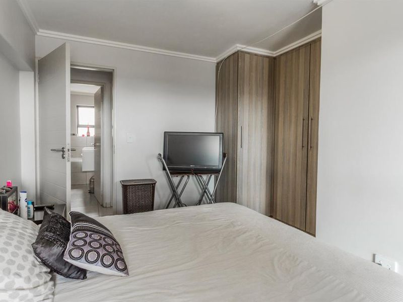 A bedroom featuring built-in wooden cupboards and access to an adjoining bathroom, finished with simple coving and neutral wall tones.