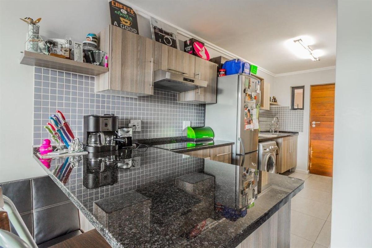 Modern kitchen featuring granite countertops, tiled backsplash, built-in cabinetry, and an integrated extractor fan with a breakfast bar area.