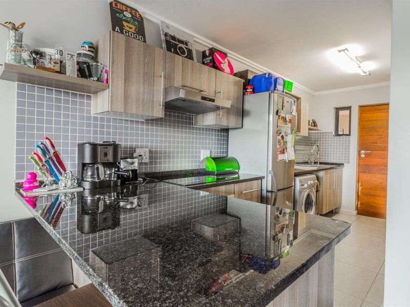 Modern kitchen featuring granite countertops, tiled backsplash, built-in cabinetry, and an integrated extractor fan with a breakfast bar area.