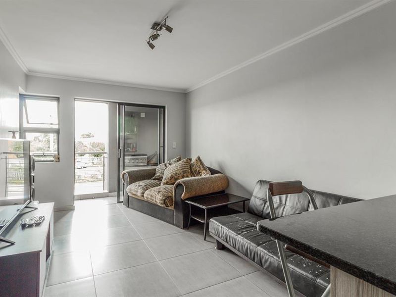 Open plan living area featuring tiled flooring, a breakfast bar, and direct access to a private balcony through sliding glass doors.