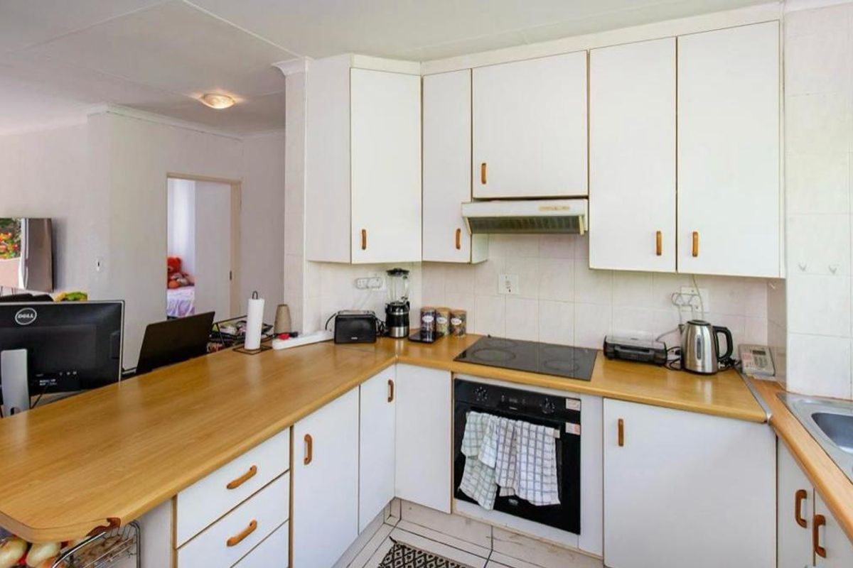 Functional kitchen featuring white cabinetry, laminate countertops, built-in oven, electric hob, and an integrated extractor fan with a breakfast bar counter.