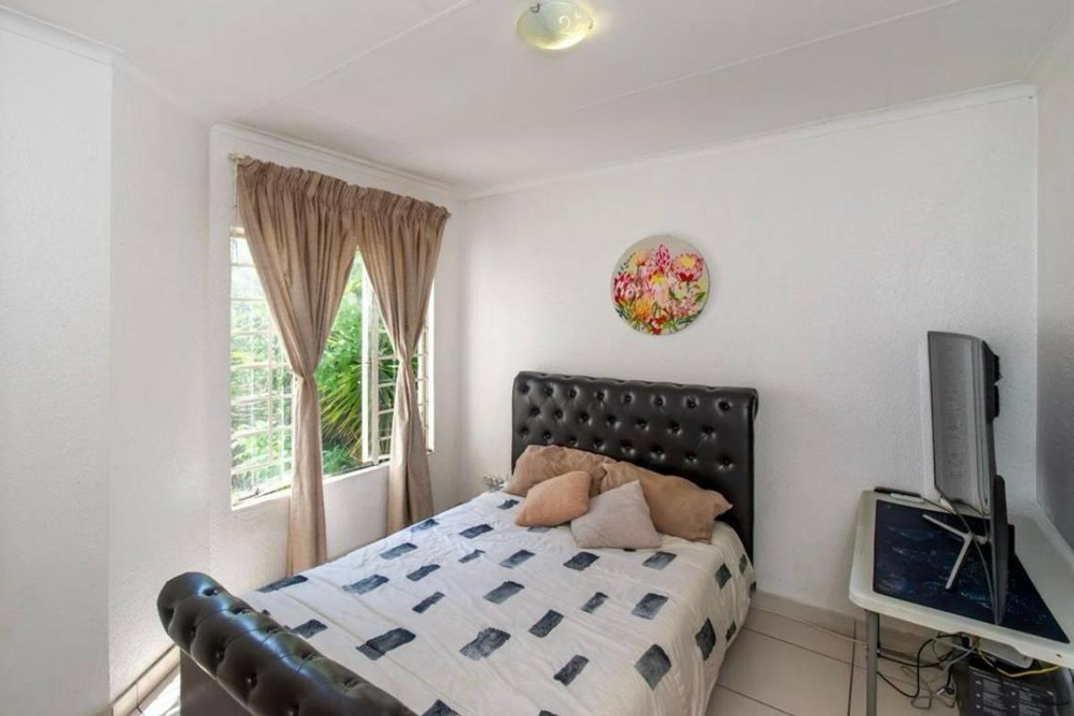 A functional bedroom featuring tiled flooring, a window with security bars, and a neutral color palette, suitable for a comfortable living space.
