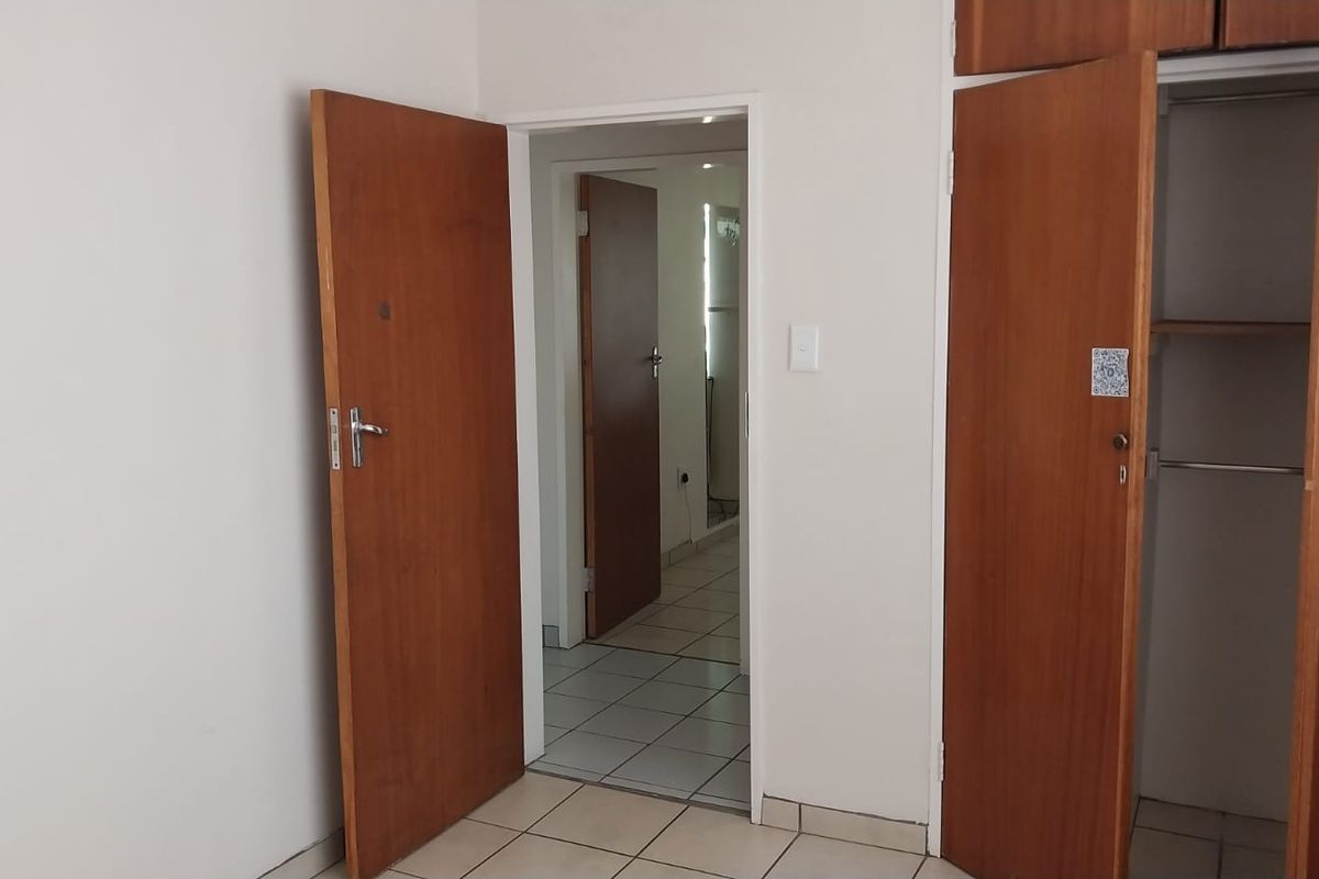 A bedroom interior featuring built-in wooden cupboards and tiled flooring, with a doorway leading to an adjacent hallway.