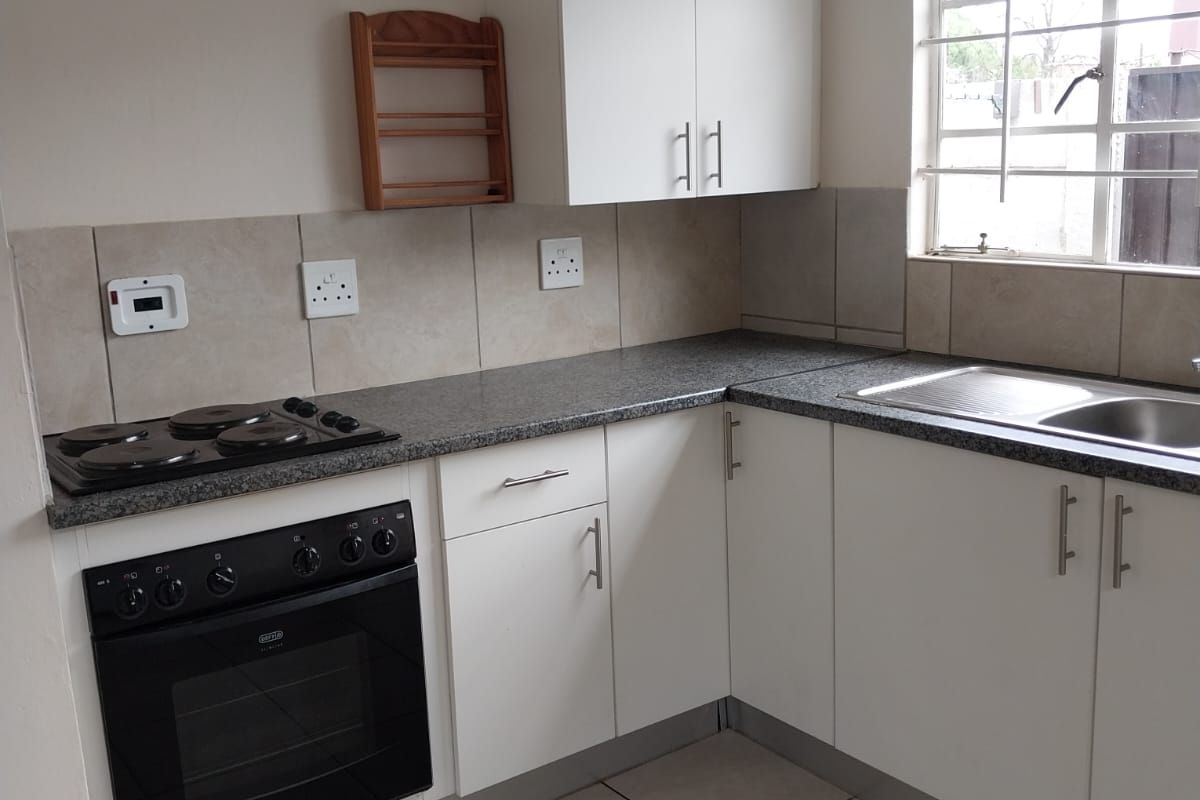 A functional kitchen featuring white cabinetry, granite countertops, a built-in oven and hob, and tiled flooring.