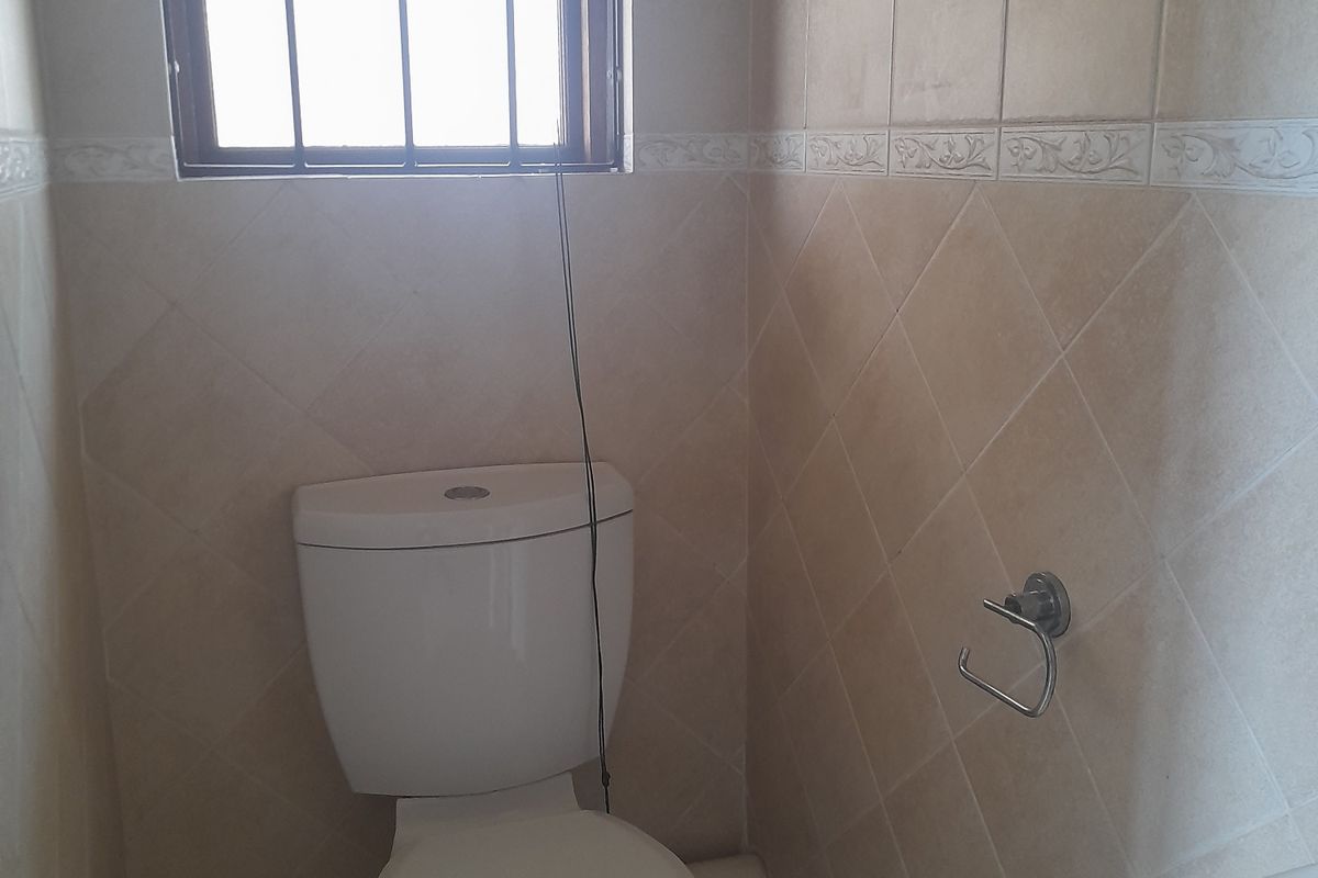 A compact guest bathroom featuring ceramic wall and floor tiles, a standard toilet, and a wall-mounted basin with a security-barred window.