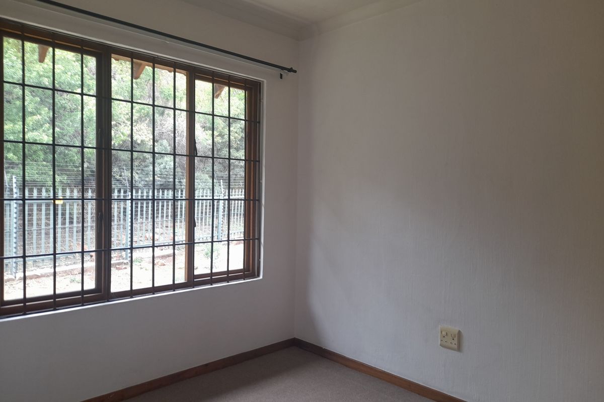 A vacant bedroom featuring neutral carpeting, a large window with security bars, and a standard electrical outlet.