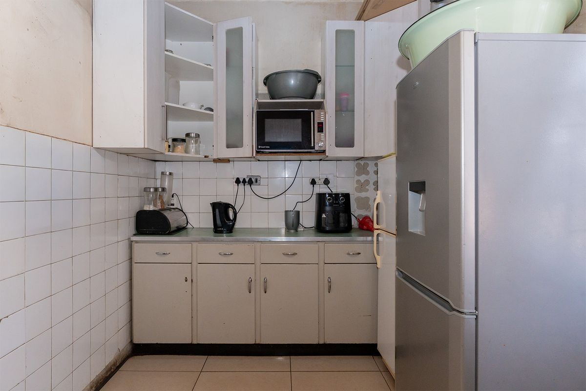 A compact kitchen featuring tiled backsplash, built-in cabinetry, and tiled flooring, currently showing signs of wear and requiring cosmetic updates.