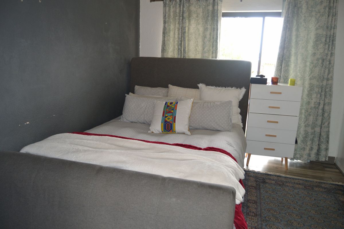 A bedroom featuring a dark accent wall, neutral flooring, and a window with curtains.