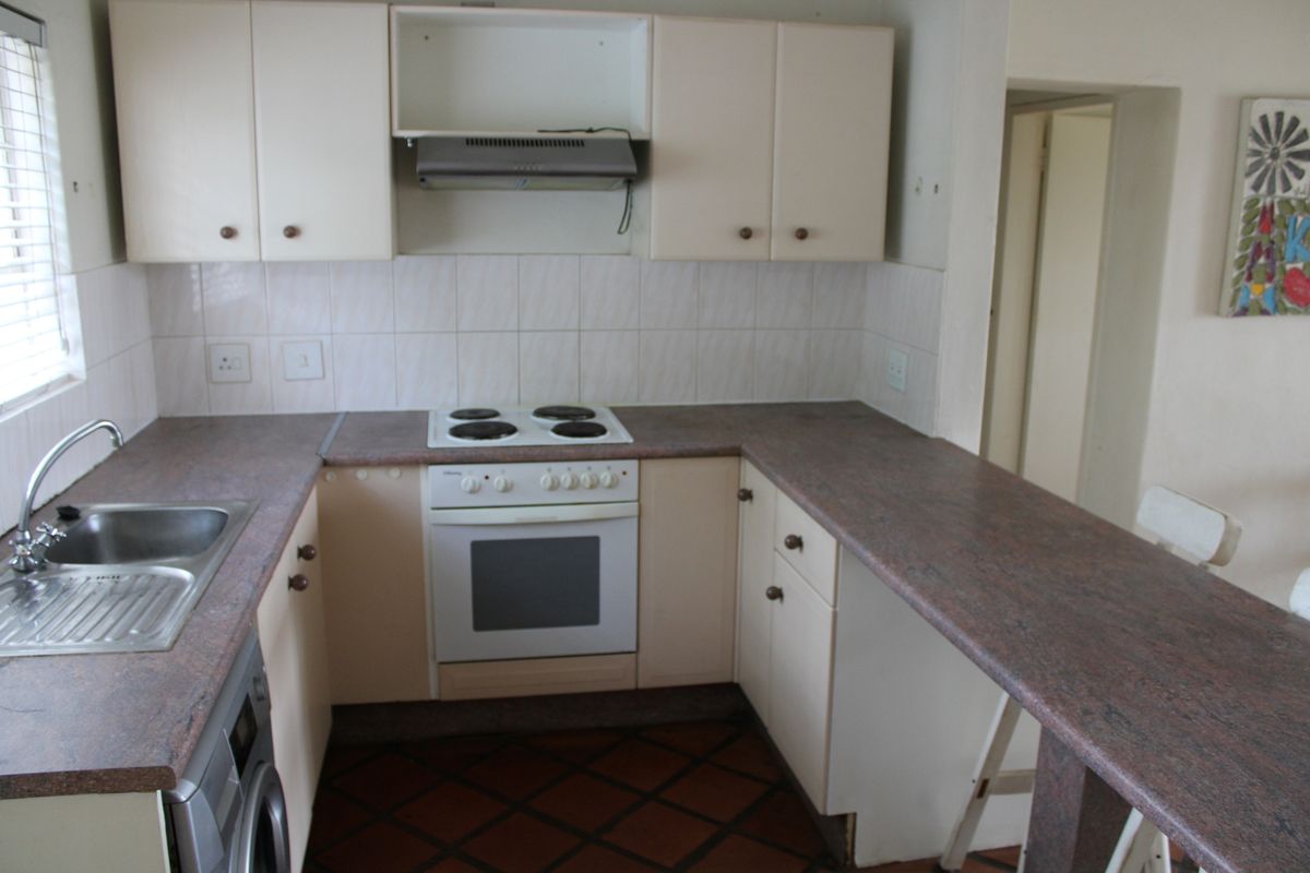 A dated kitchen featuring laminate cabinetry, a built-in electric oven and hob, and a breakfast bar counter with terracotta floor tiles.