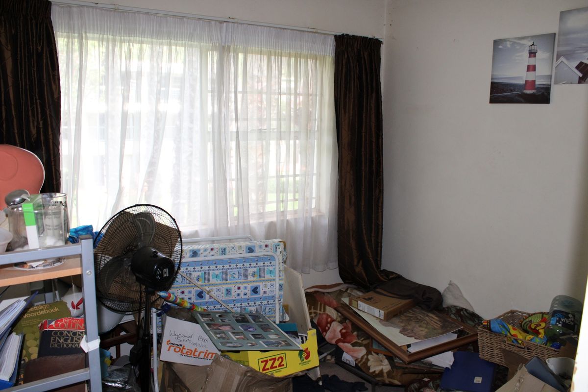A bedroom space featuring a window with curtain tracks, currently cluttered with personal belongings.