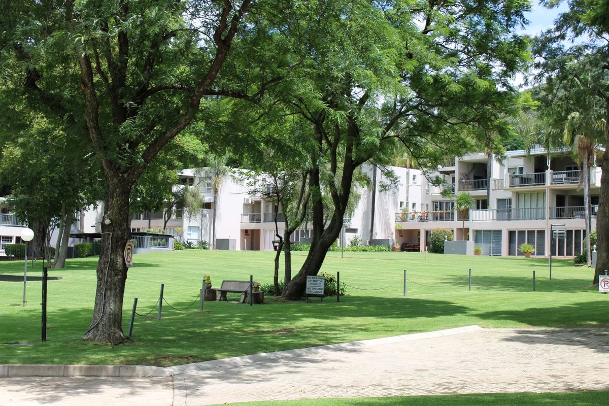 A view of the townhouse complex featuring a well-maintained communal lawn, mature trees, and multi-level residential units with private balconies.