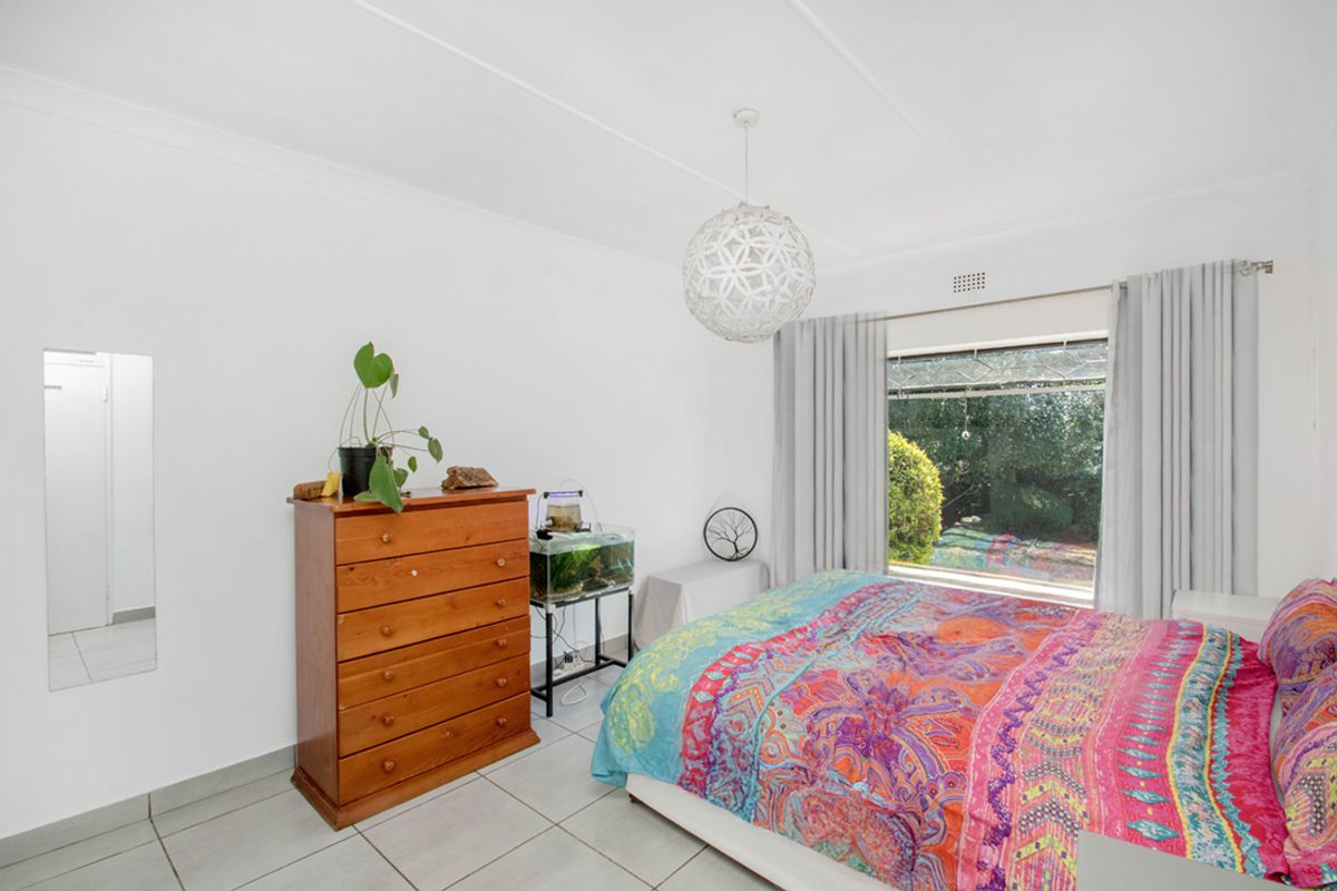 A bright bedroom featuring tiled flooring, neutral walls, and a large window overlooking the garden.