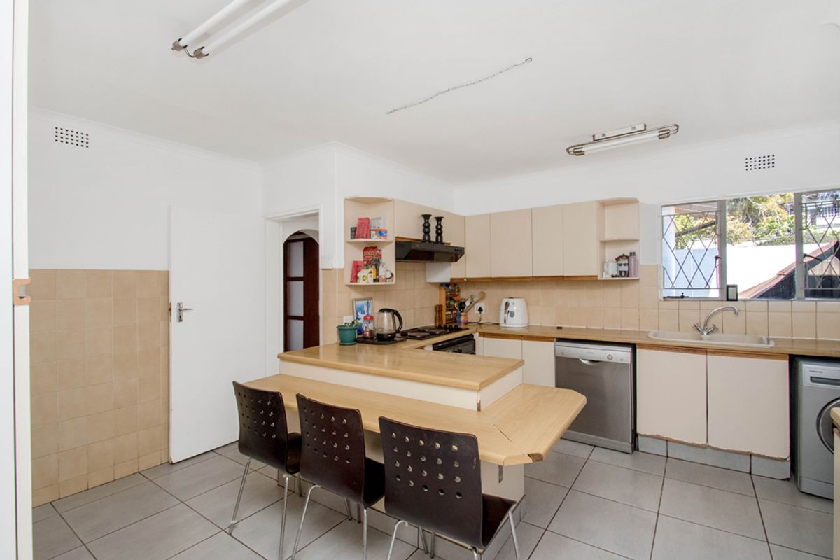 Functional kitchen featuring laminate countertops, built-in cabinetry, tiled splashbacks, and a breakfast bar area with tiled flooring.