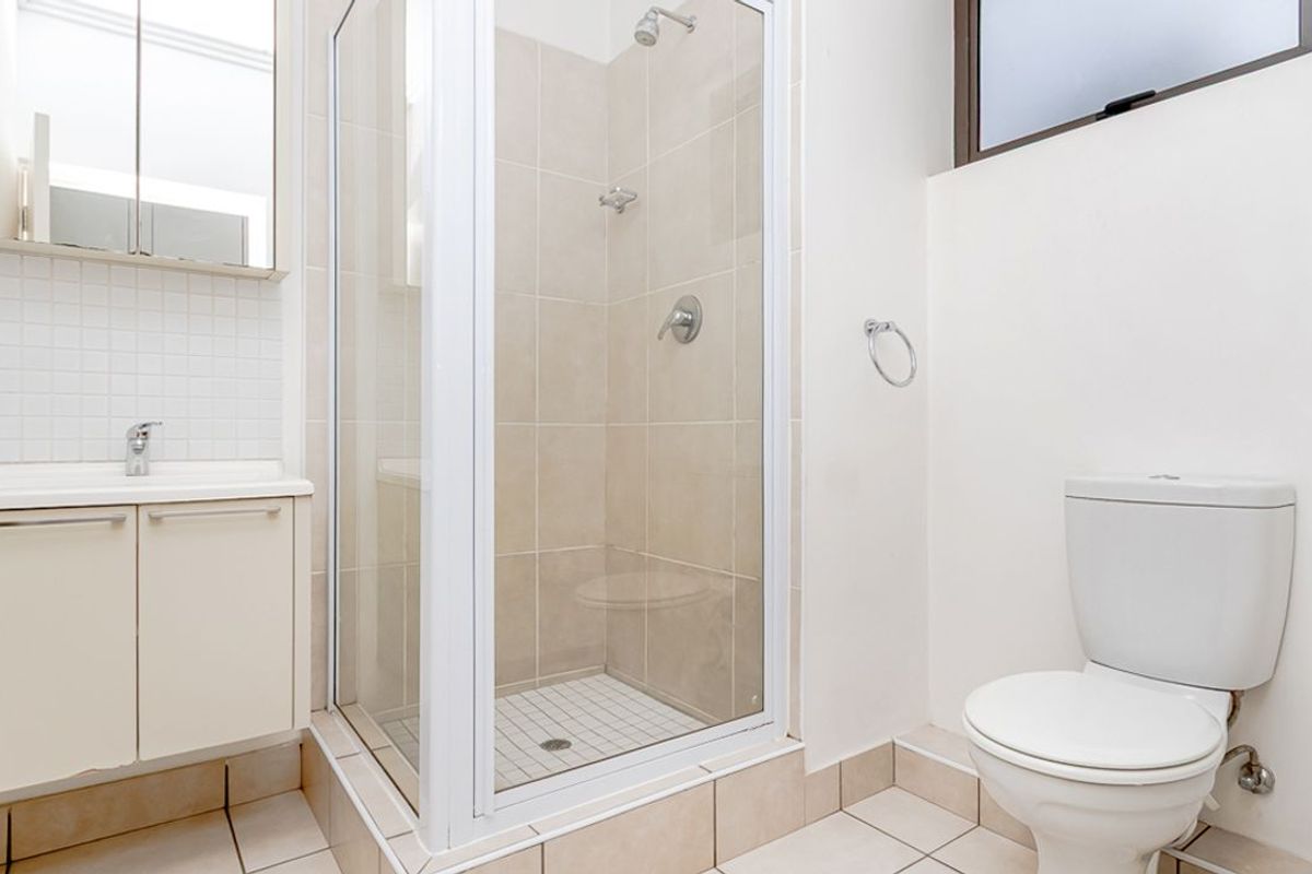 A functional bathroom featuring a glass-enclosed shower, a vanity with integrated basin, and a standard toilet.