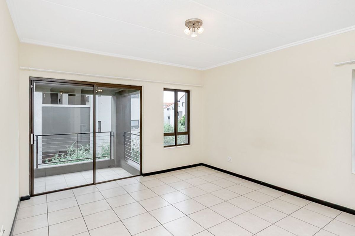 A bright, empty living room featuring tiled flooring, a ceiling light fixture, and sliding glass doors leading to a private balcony.