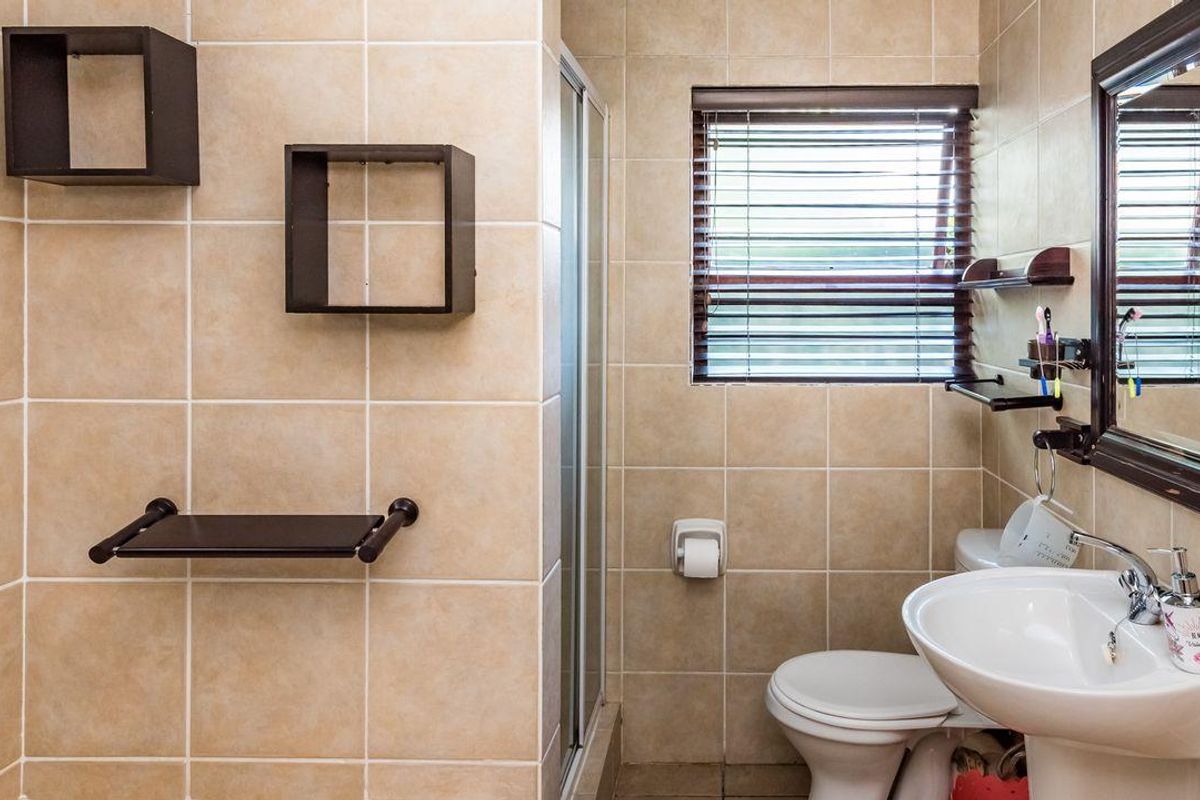 A functional bathroom featuring beige wall tiles, a pedestal basin, a toilet, and a glass-enclosed shower stall with a window for natural light.