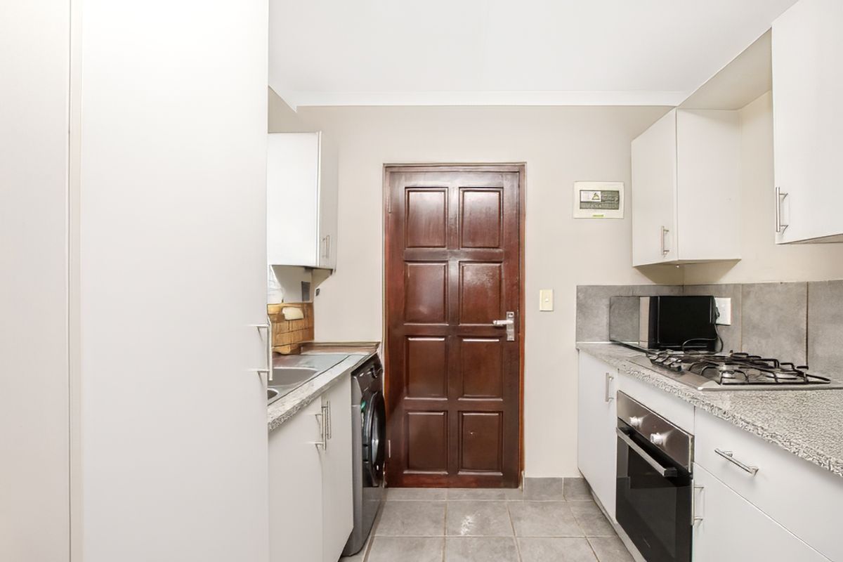 Compact kitchen featuring white cabinetry, granite countertops, built-in oven, gas hob, and dedicated space for a washing machine.