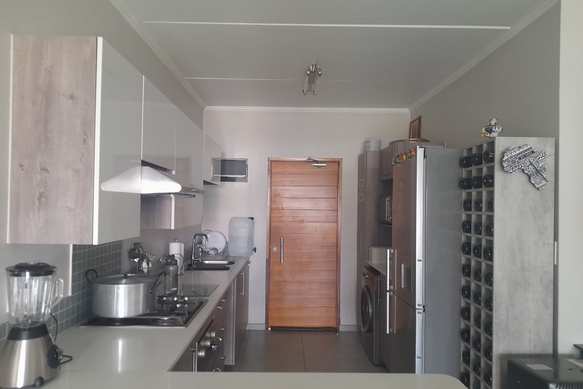 Modern kitchen featuring sleek cabinetry, integrated gas hob, extractor fan, and tiled flooring, leading to a wooden door entrance.