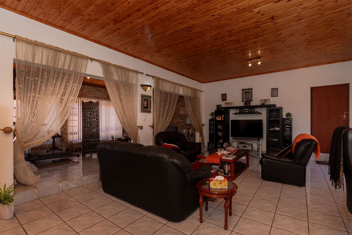 Spacious living room featuring a timber tongue and groove ceiling, ceramic tiled flooring, and an exposed brick feature wall.