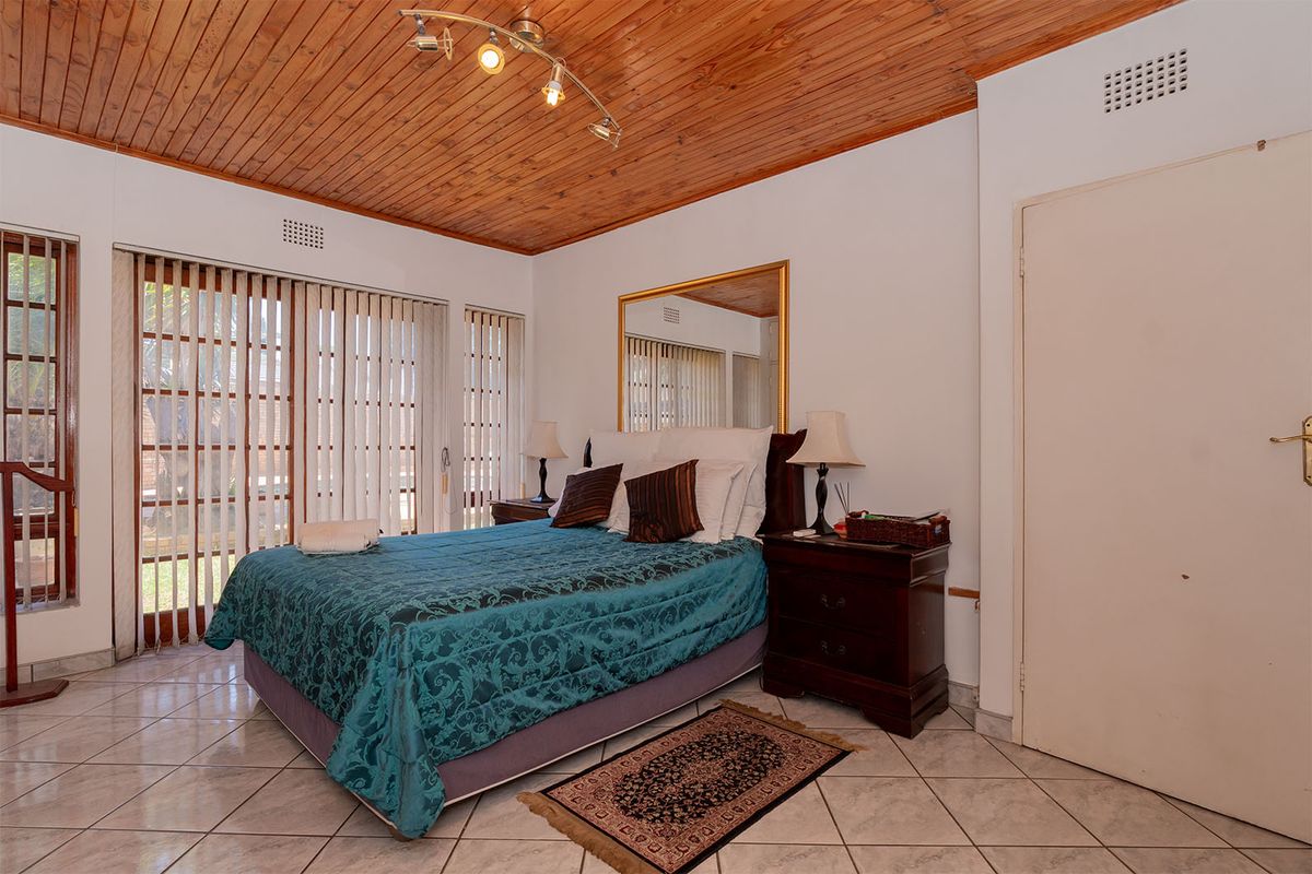 A bedroom featuring a timber-clad ceiling, tiled flooring, and large sliding glass doors with vertical blinds providing natural light.