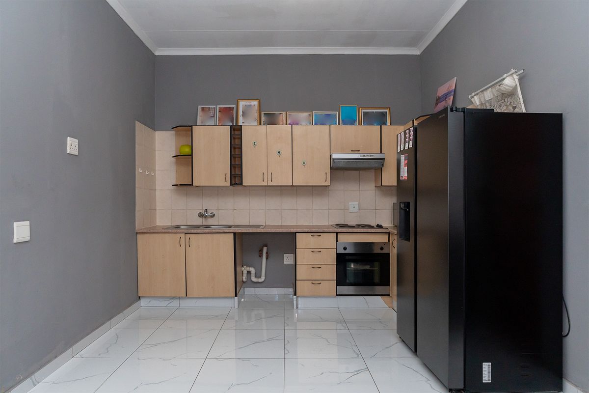 A functional kitchen featuring light wood cabinetry, tiled backsplash, built-in oven, extractor fan, and modern white marble-look floor tiles.