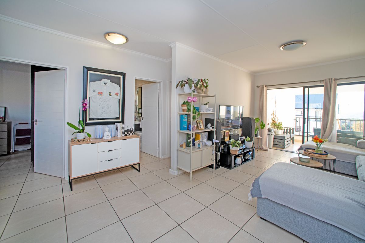 A bright living room featuring neutral tiled flooring, flush mount lighting, and direct access to an outdoor balcony through sliding glass doors.