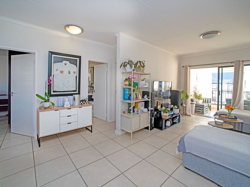 A bright living room featuring neutral tiled flooring, flush mount lighting, and direct access to an outdoor balcony through sliding glass doors.