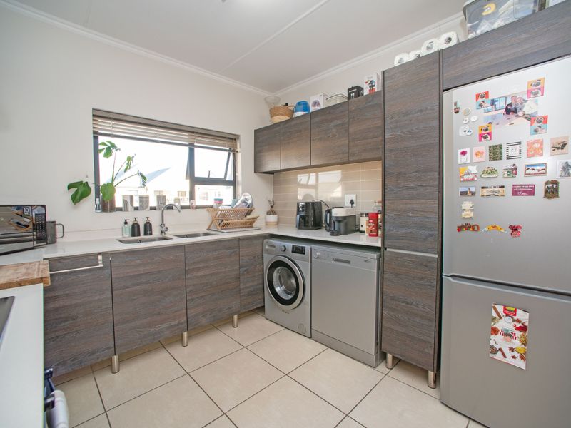 A functional kitchen featuring modern wood-grain cabinetry, tiled flooring, integrated appliances, and a window providing natural light over the sink area.