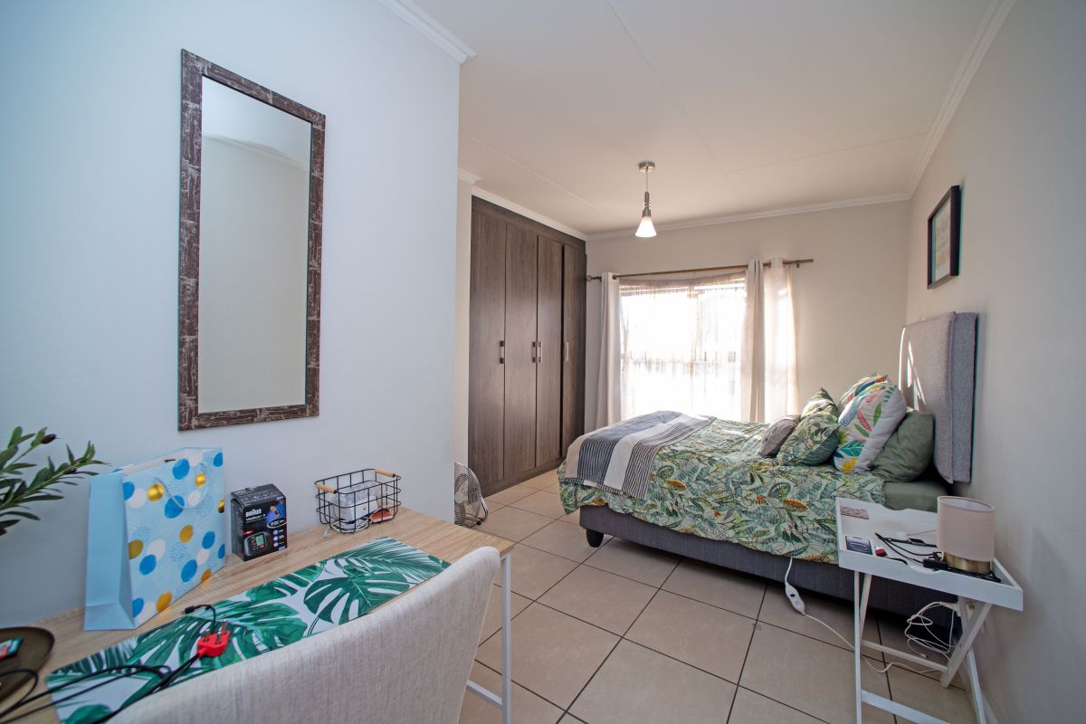 A well-maintained bedroom featuring built-in cupboards, neutral tiled flooring, and natural light from the window.