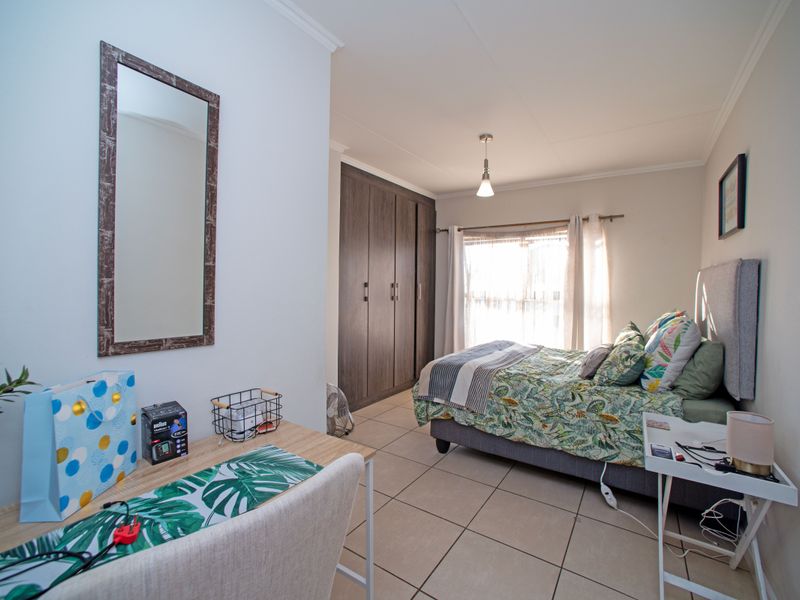 A well-maintained bedroom featuring built-in cupboards, neutral tiled flooring, and natural light from the window.