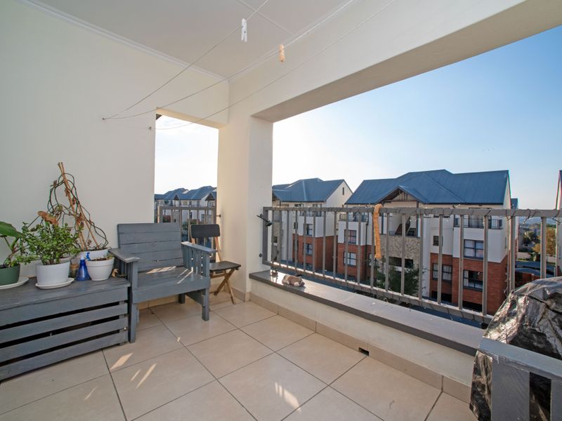 A covered balcony featuring tiled flooring and a metal balustrade, offering an open view of the surrounding apartment complex.