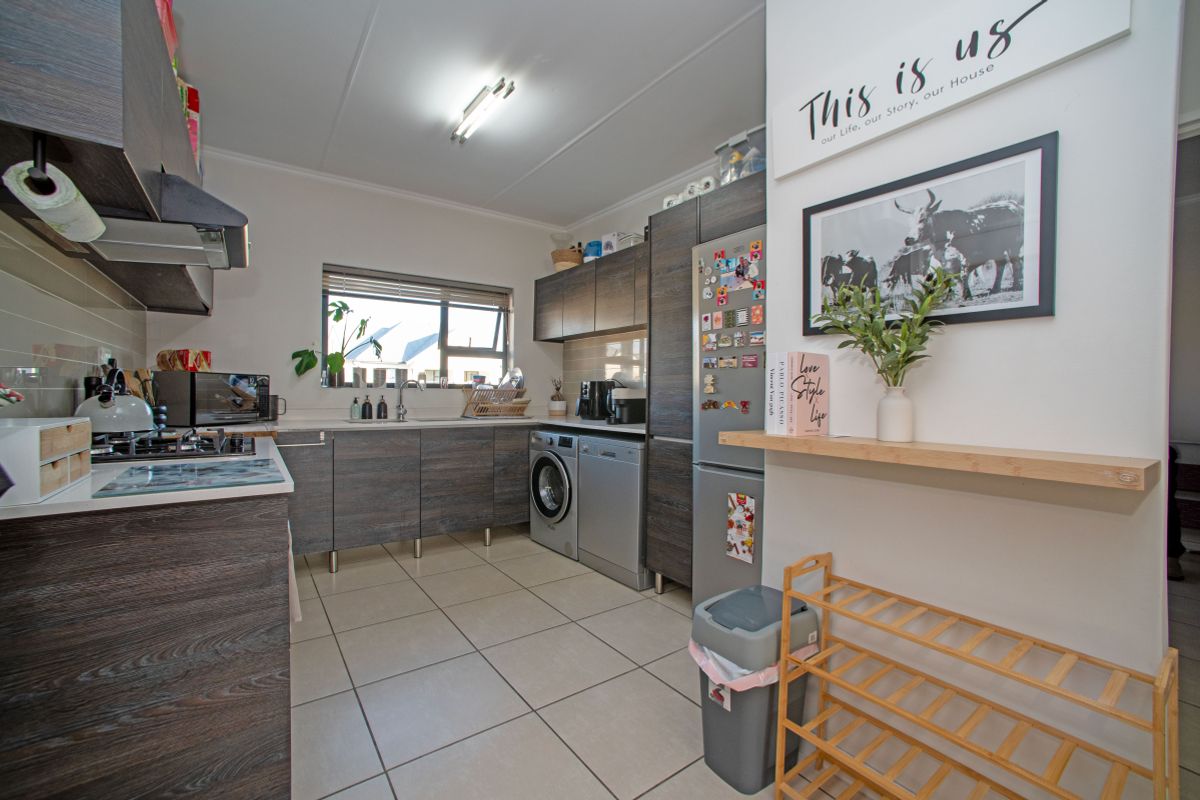 Modern kitchen featuring dark wood-grain cabinetry, gas hob, extractor fan, and integrated laundry plumbing with tiled flooring and ample counter space.