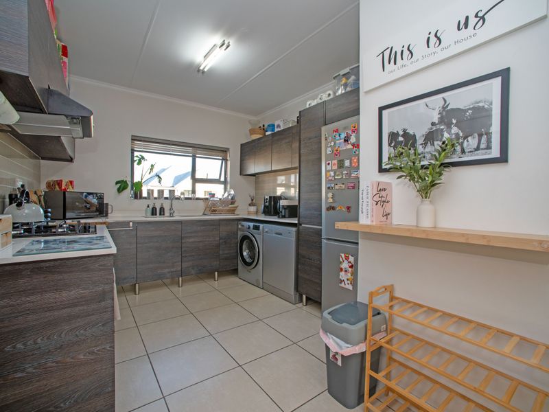 Modern kitchen featuring dark wood-grain cabinetry, gas hob, extractor fan, and integrated laundry plumbing with tiled flooring and ample counter space.