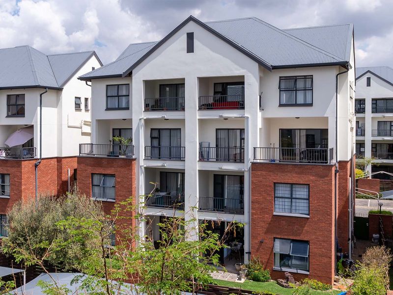 A multi-story apartment building featuring a combination of brick and white plaster finishes, with private balconies and a pitched corrugated metal roof.