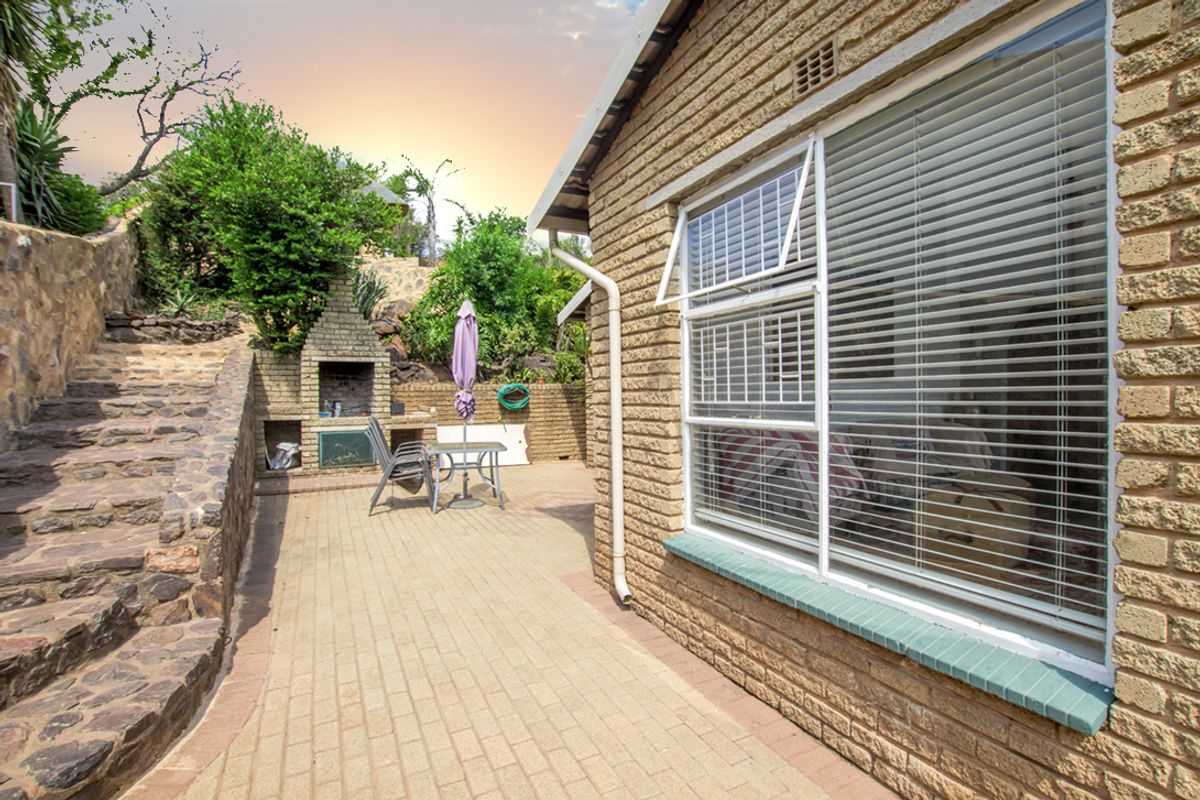 Rear exterior area featuring brick paving, a built-in braai, stone retaining walls, and a brick facade with aluminium window frames.