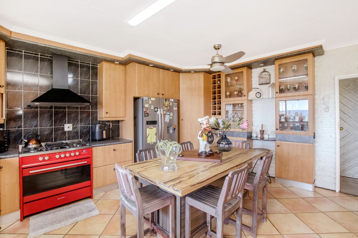 A functional kitchen featuring light wood cabinetry, a red gas stove with extractor, tiled flooring, and a central dining island with integrated seating.