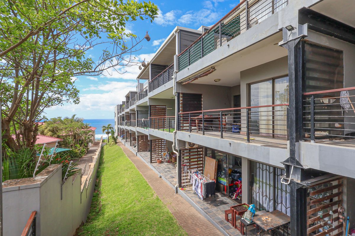 Exterior view of a multi-story apartment complex featuring private balconies, metal railings, and a landscaped garden area with ocean views.