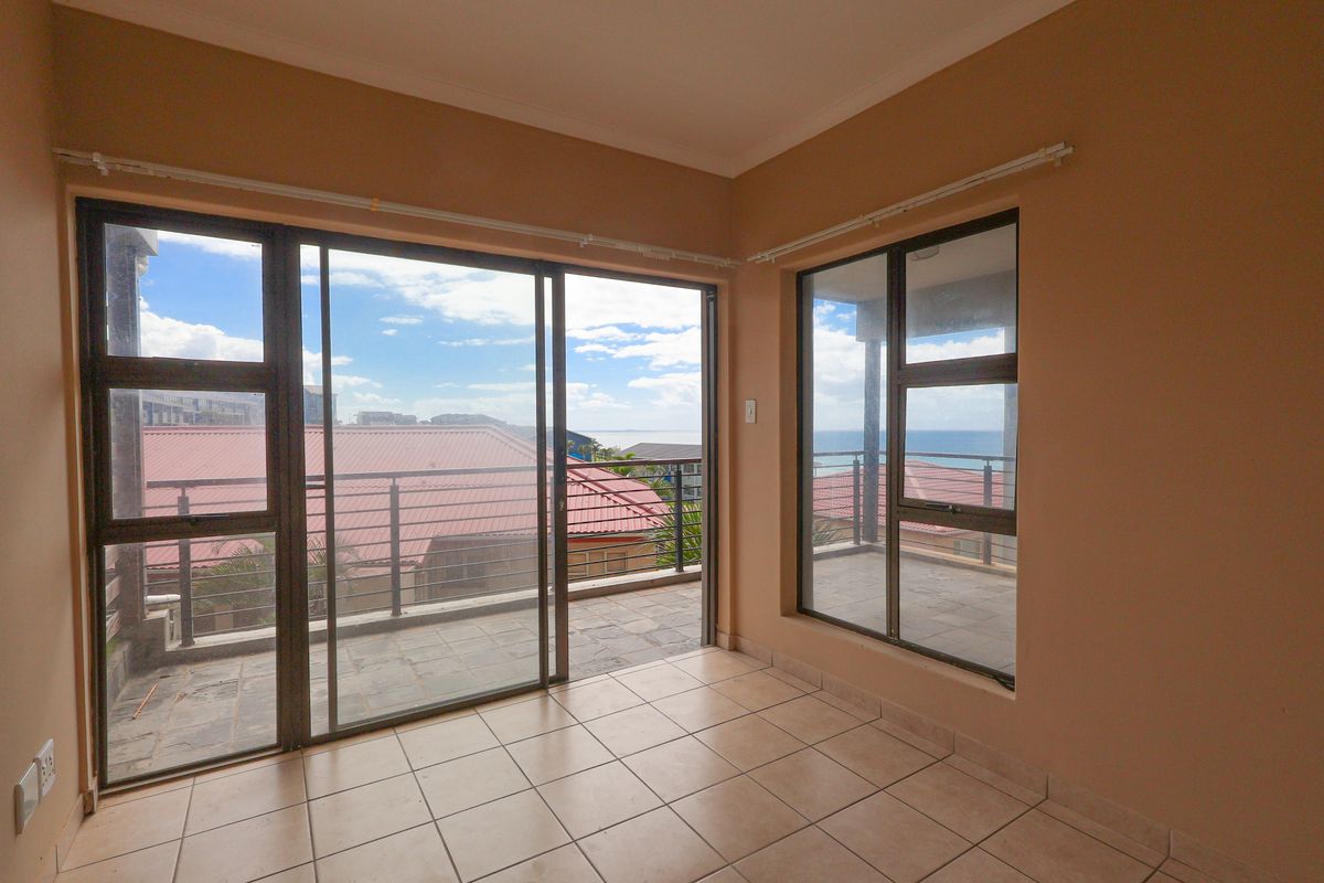 A bright, empty living area featuring large sliding glass doors that open onto a spacious balcony with scenic coastal views.