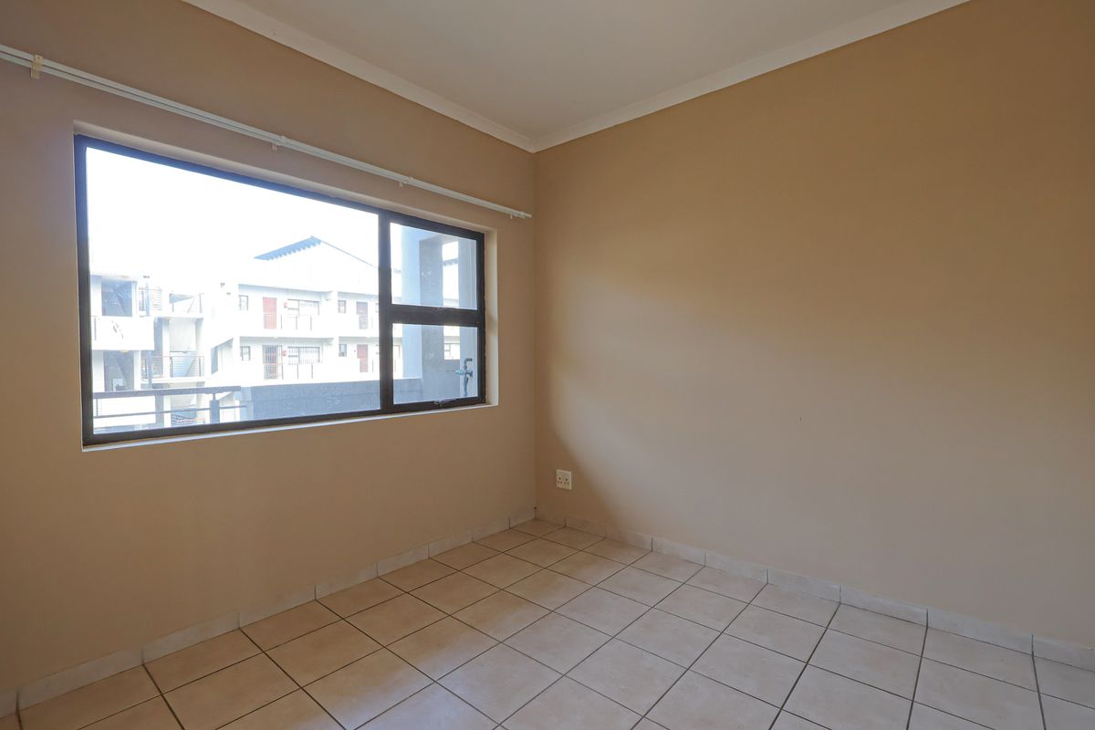 A bright, empty bedroom featuring neutral wall paint, tiled flooring, and a large window providing natural light.