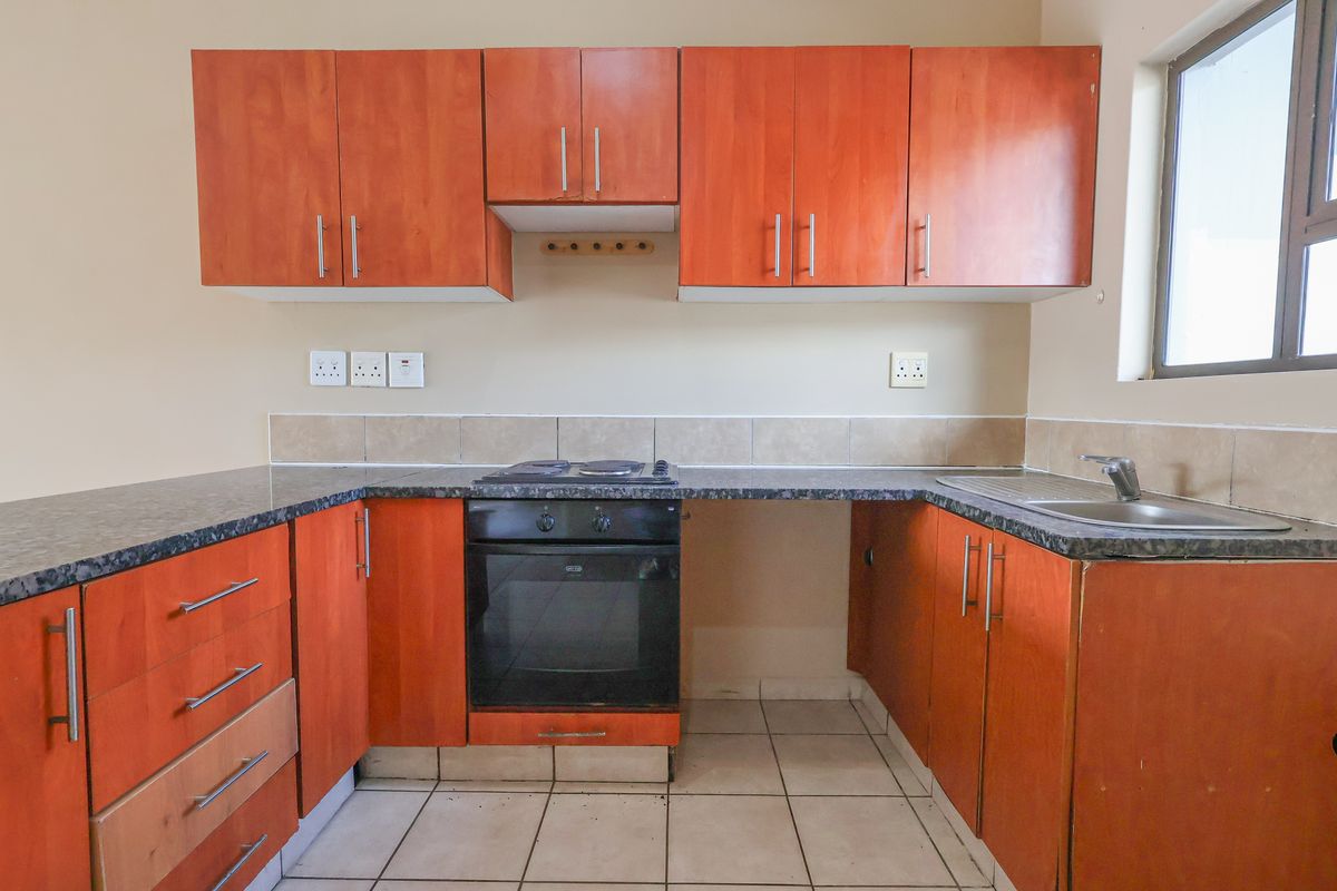 A functional kitchen featuring wooden cabinetry, a built-in oven, electric hob, and a stainless steel sink with tiled splashbacks.
