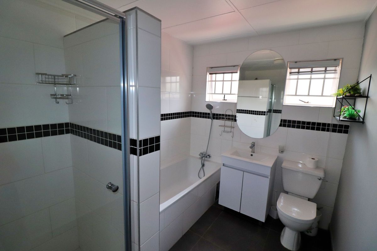 A clean, functional bathroom featuring a separate glass shower enclosure, a bathtub, a vanity basin, and a toilet with classic white and black tile accents.