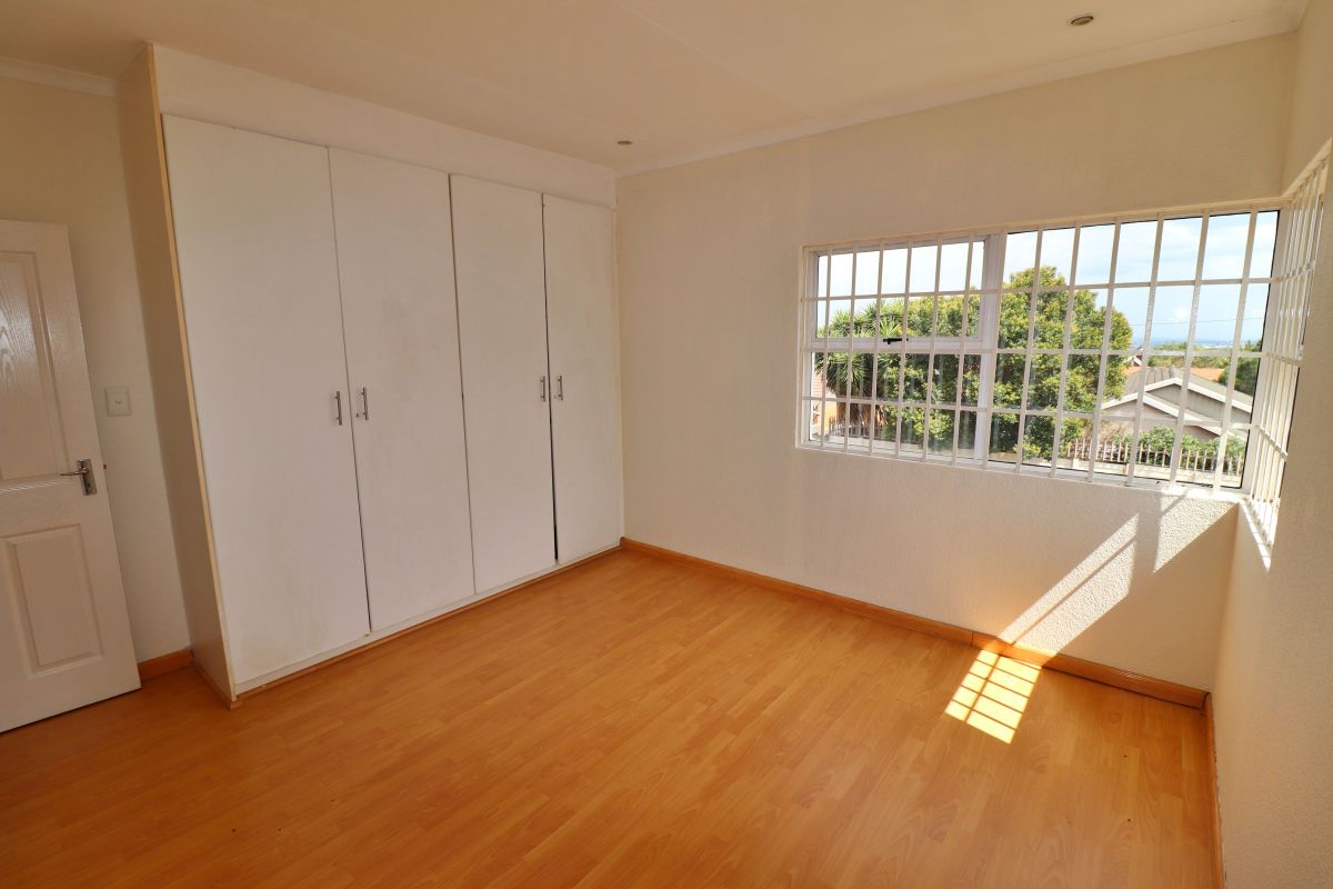 A bright, empty bedroom featuring built-in wardrobes, laminate wood flooring, and a window fitted with security bars.