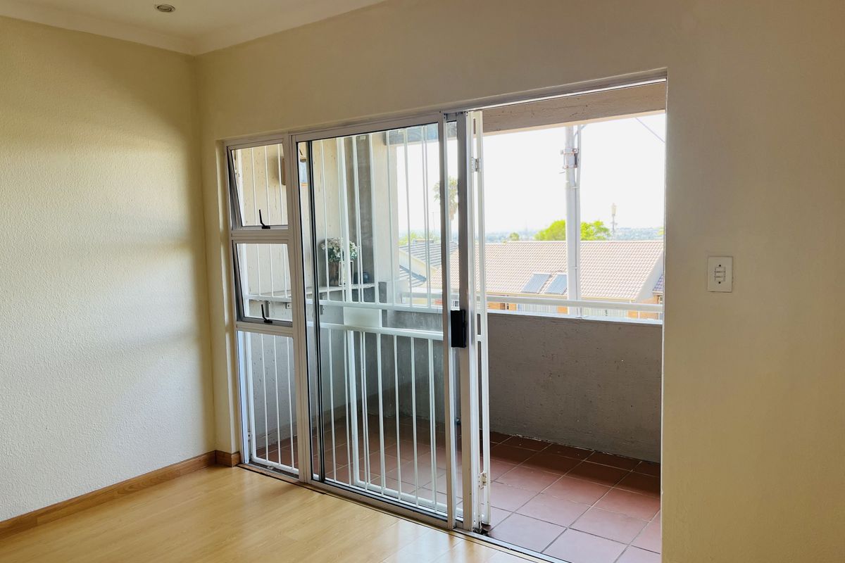 A bright living area featuring laminate flooring and large sliding glass doors that open onto a private balcony with security bars.