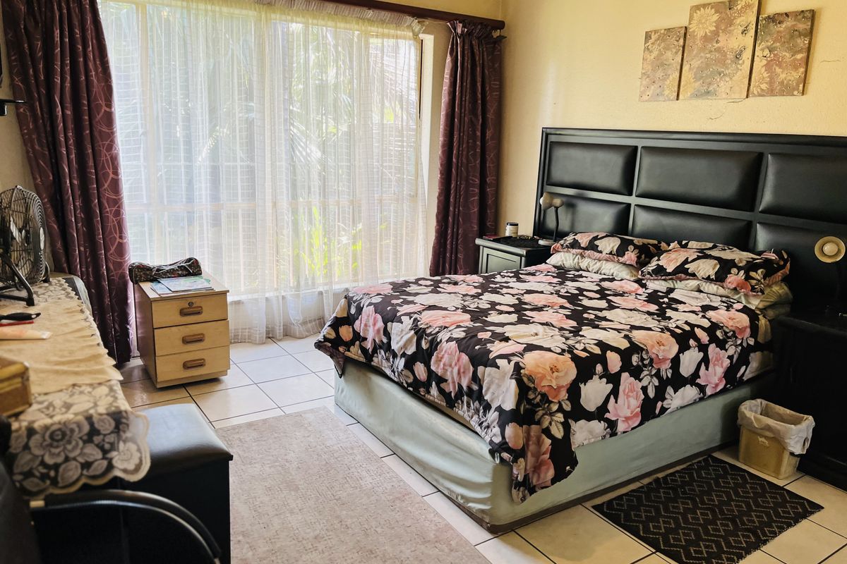 A spacious bedroom featuring large windows with natural light, tiled flooring, and a built-in headboard structure.