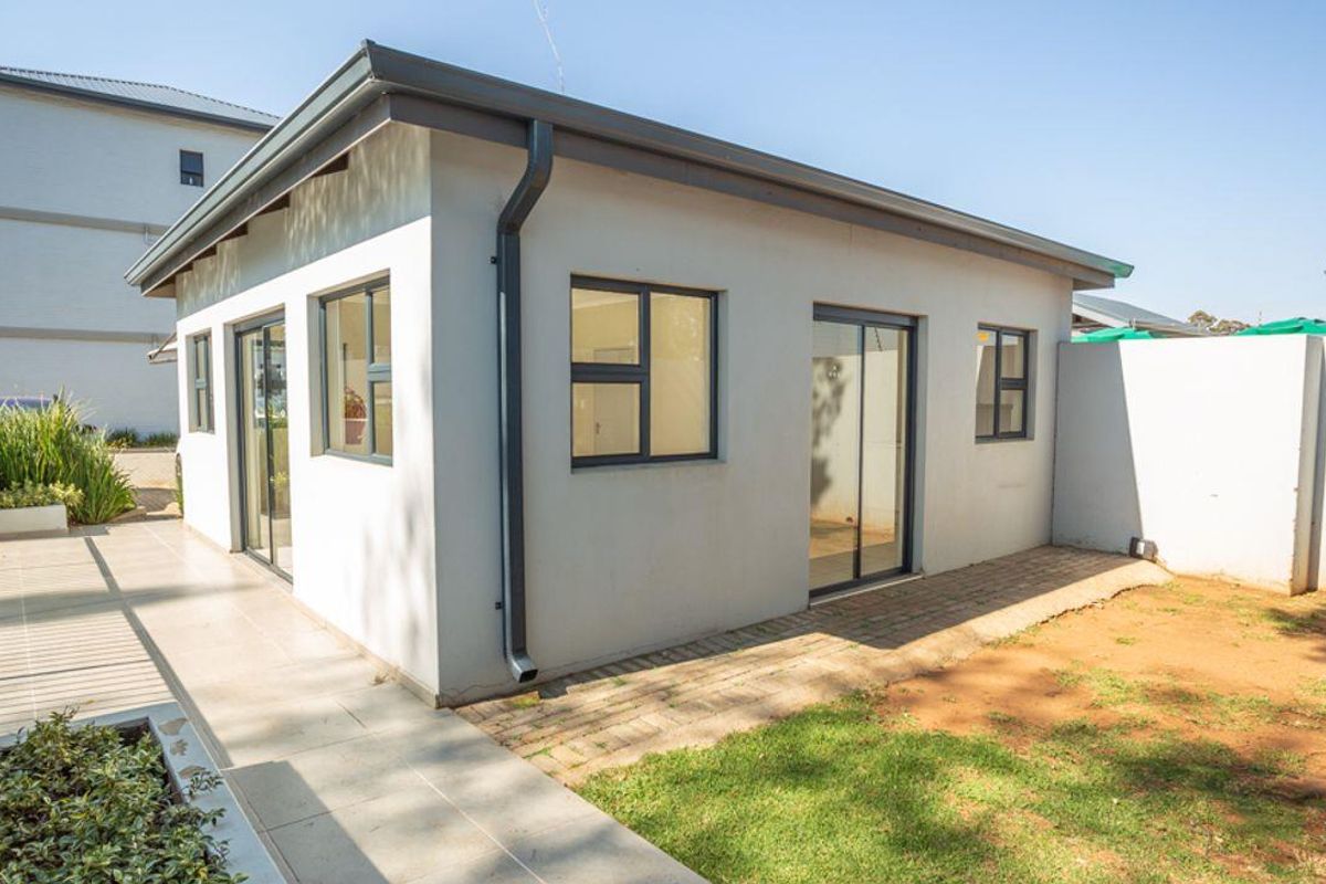 Exterior view of a modern apartment unit featuring a paved walkway, sliding glass doors, and a private garden area.