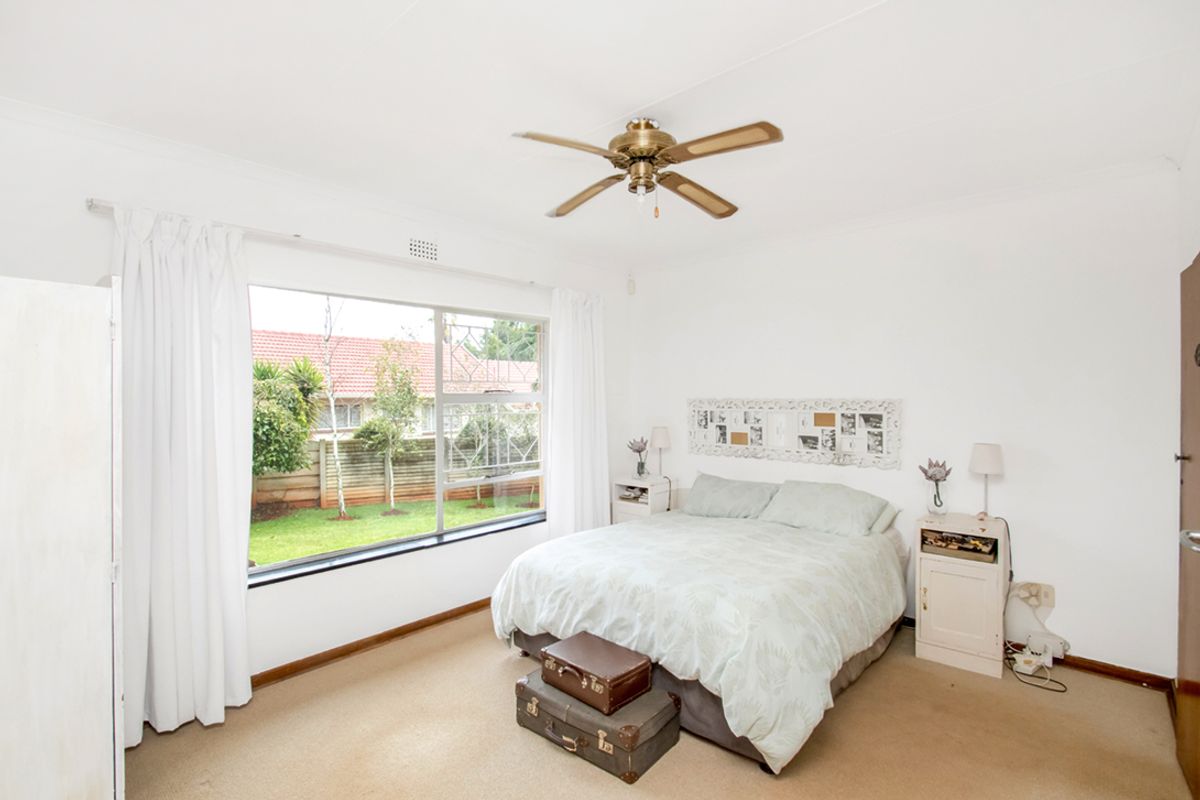 A bright bedroom featuring a large window with garden views, neutral walls, and a ceiling fan.