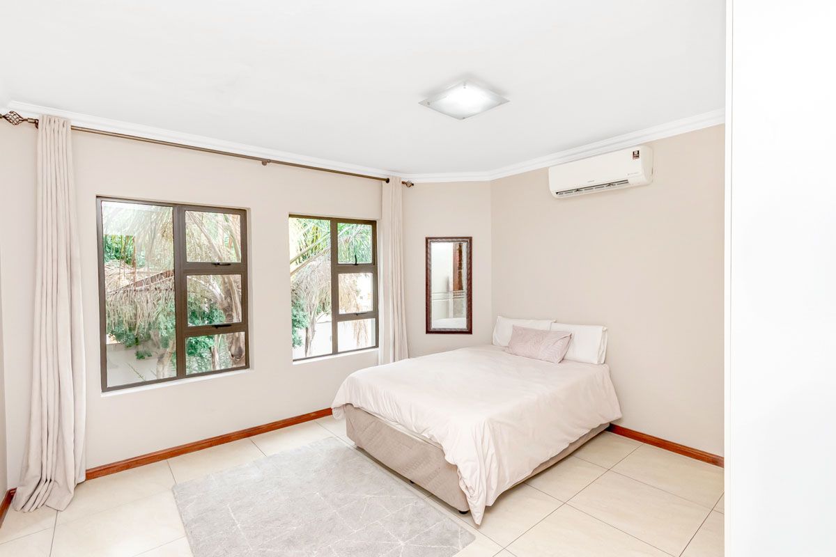 A bright and spacious bedroom featuring tiled flooring, large windows, and a wall-mounted air conditioning unit.
