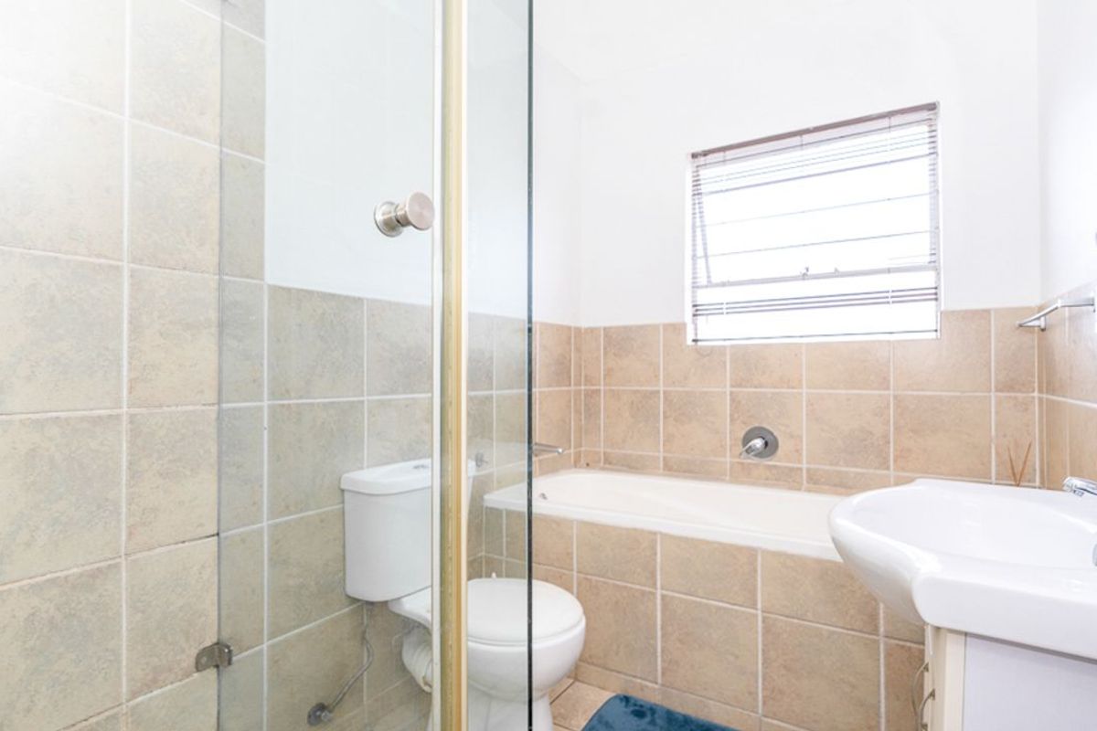 A functional bathroom featuring a built-in bathtub, a separate glass-enclosed shower, a pedestal basin, and neutral wall tiling.