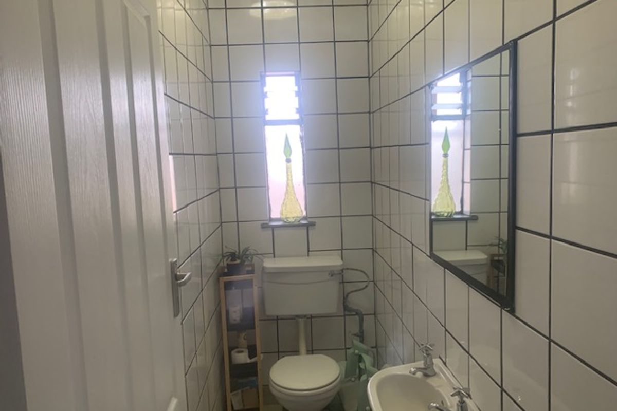 A compact guest bathroom featuring full-height white ceramic wall tiles, a pedestal basin, and a standard toilet.