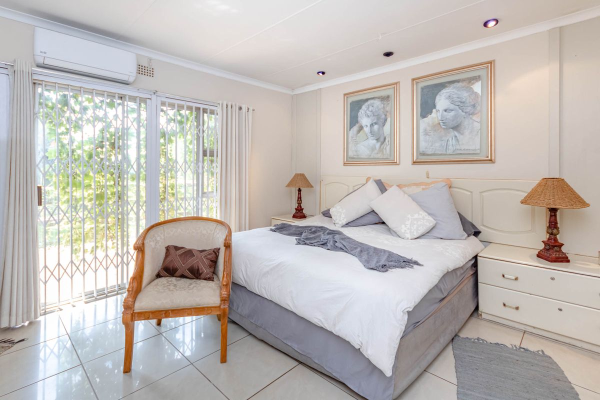 A well-maintained bedroom featuring tiled flooring, a built-in headboard, recessed ceiling lighting, and a sliding door with security gate leading to the exterior.